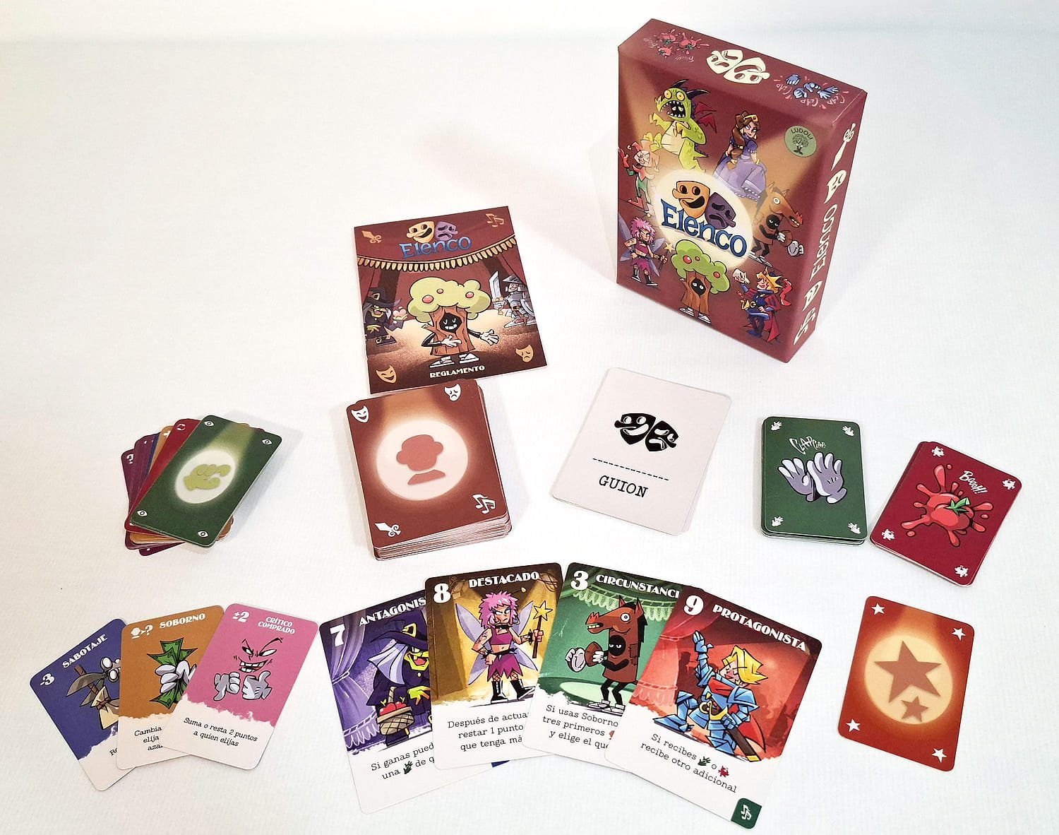 Todo el material de la nueva edición sobre la mesa: la caja, el reglamento, el mazo de Personajes, la carta de Guion y las cartas de Acción, Ovación y Abucheo